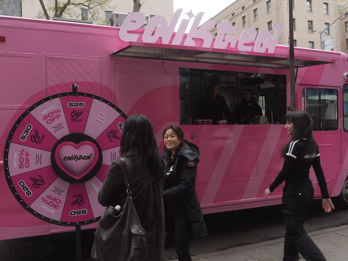 Pink retail-brand food truck with a prize wheel drawing a sidewalk crowd